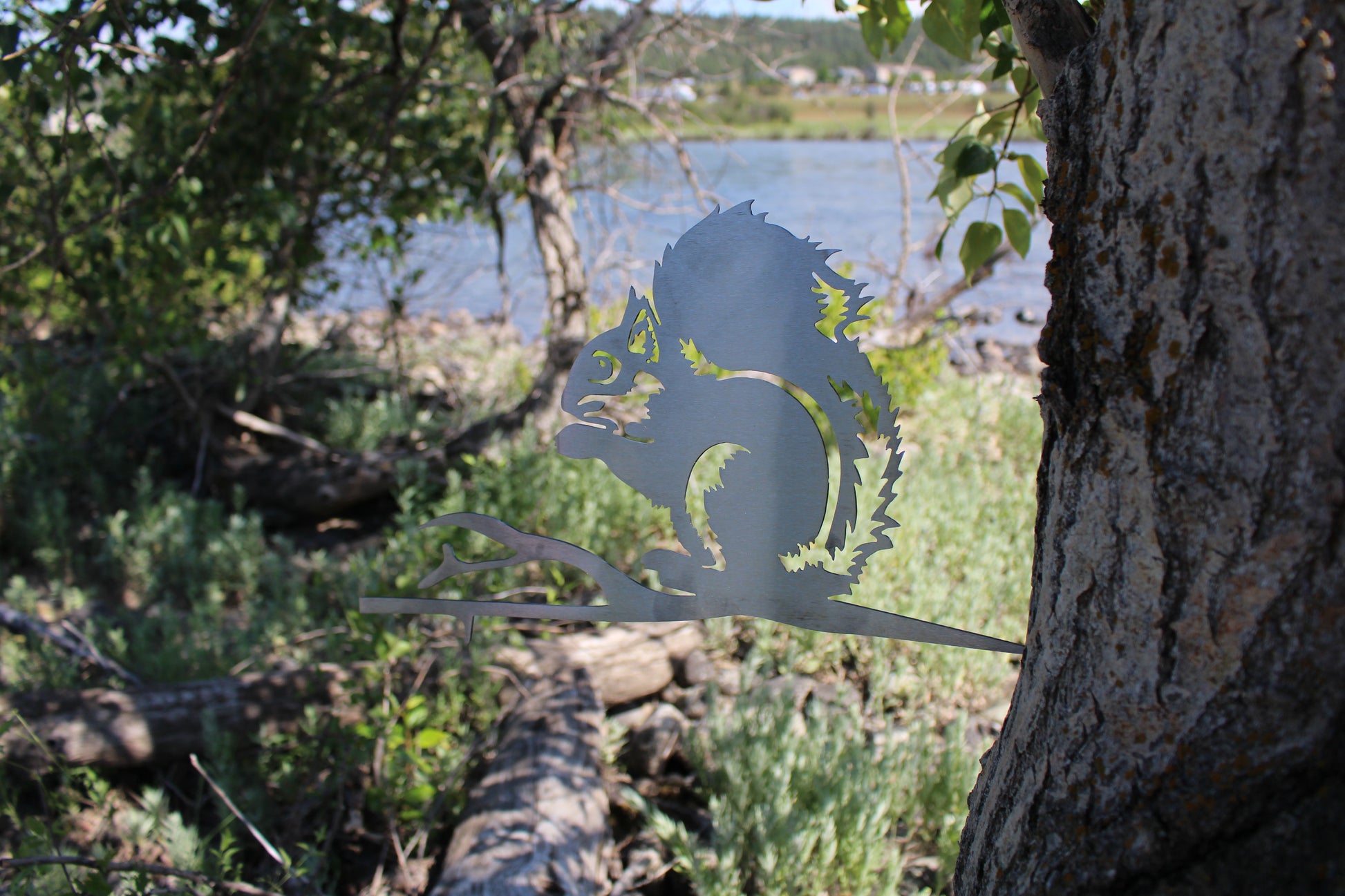 Metal squirrel tree stake on branch, rustic steel garden decoration for outdoor yard or flower bed