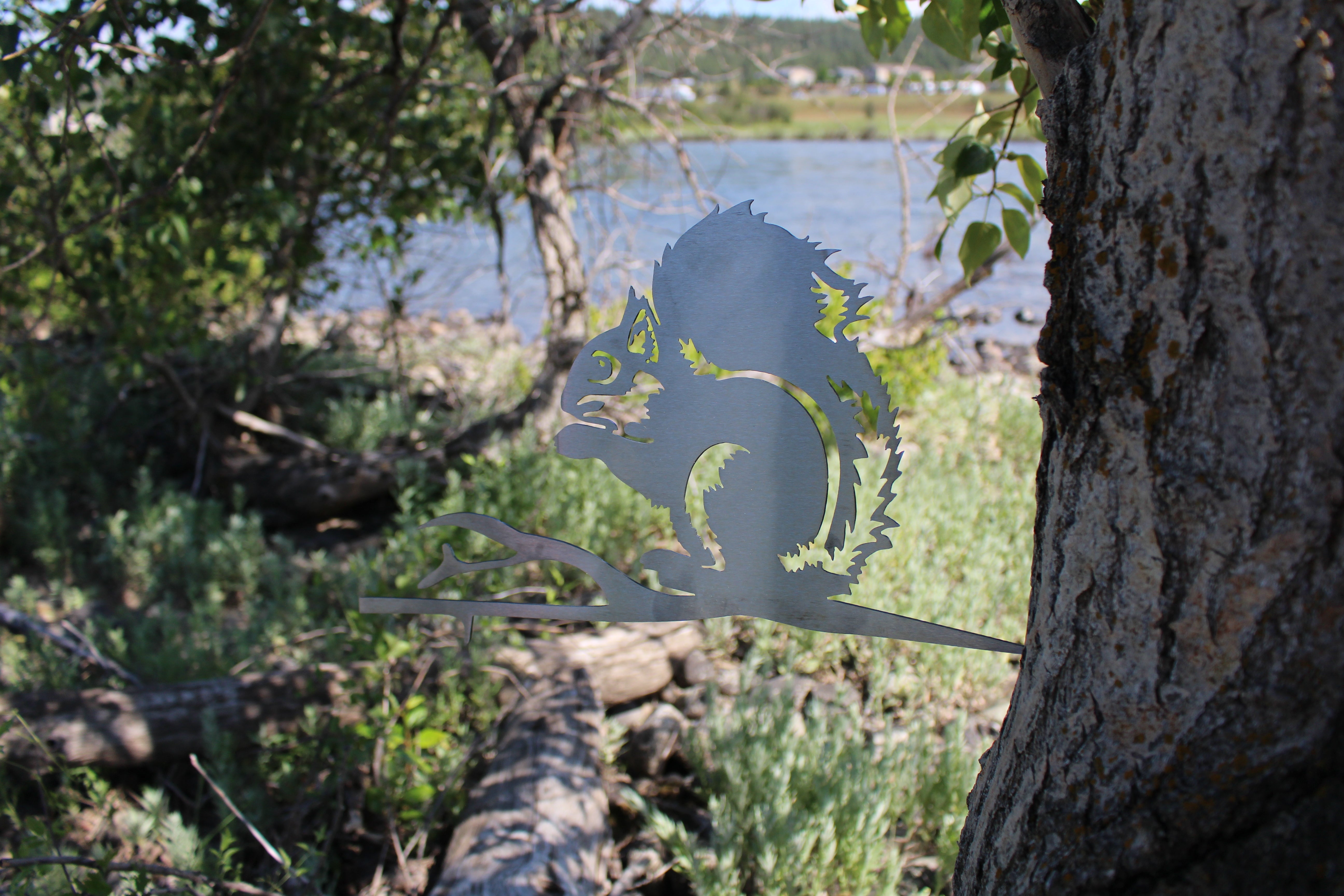 Metal squirrel tree stake on branch, rustic steel garden decoration for outdoor yard or flower bed