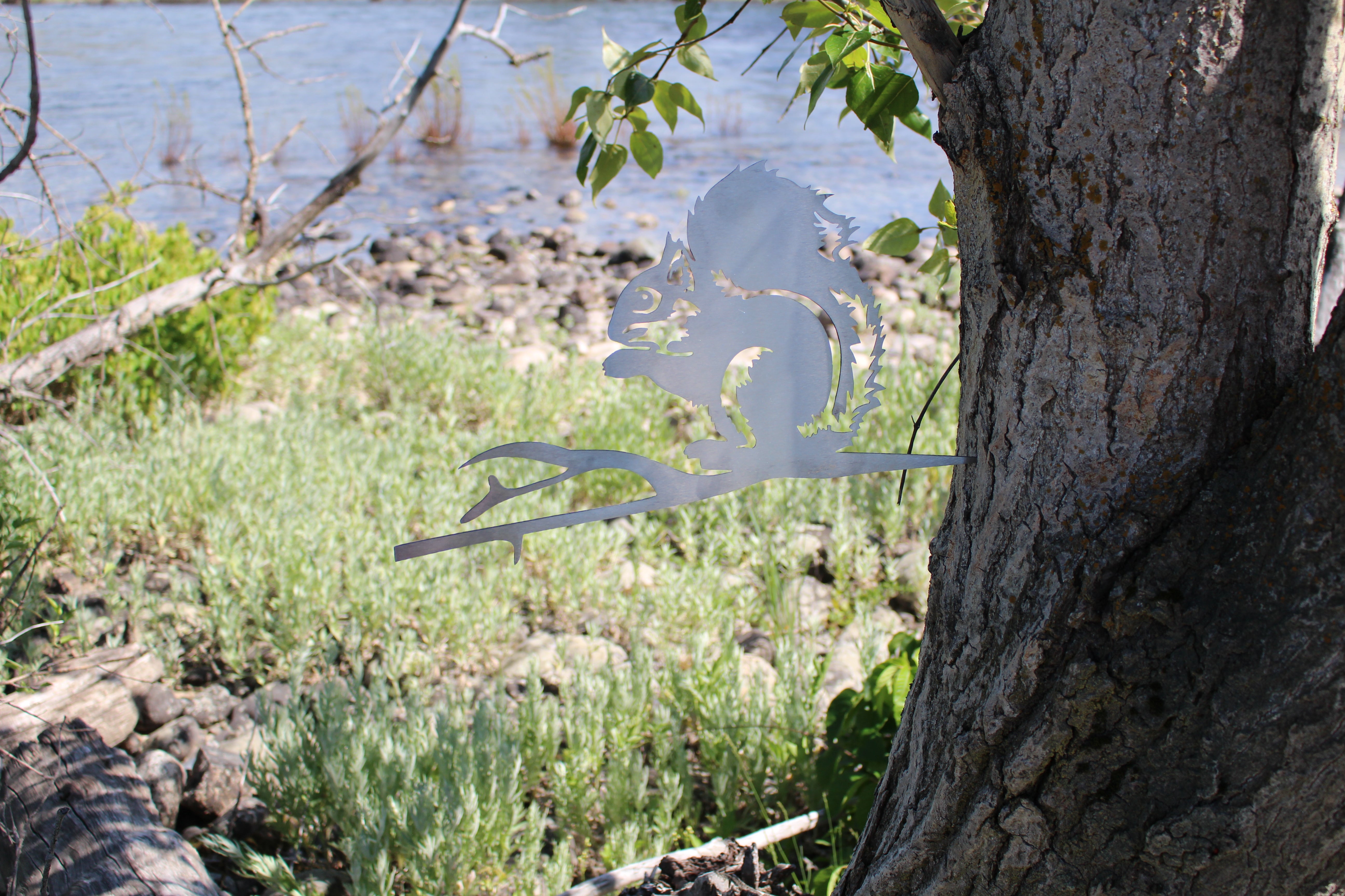 Metal squirrel tree stake on branch, rustic steel garden decoration for outdoor yard or flower bed